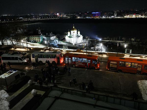 Eine Reihe von Bussen steht vor der Kulisse einer historischen russischen Stadt mit einer angestrahlten orthodoxen Kirche.