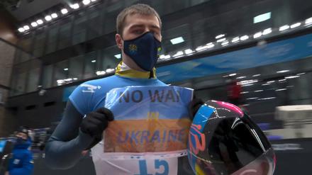 Ein Blatt Papier in einer Klarsichtfolie, DIN A4-Format, blau, gelb. In Großbuchstaben protestierte Vladyslav Heraskevych gegen die Kriegspläne der Russen.
