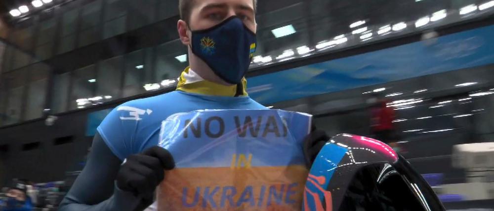 Ein Blatt Papier in einer Klarsichtfolie, DIN A4-Format, blau, gelb. In Großbuchstaben protestierte Vladyslav Heraskevych gegen die Kriegspläne der Russen.