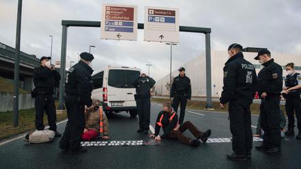 Bundespolizisten stehen am Flughafen BER vor Klimaschutz-Aktivisten der Initiative "Aufstand der letzten Generation", die eine Zufahrt zum Hauptstadt-Flughafen BER blockieren.