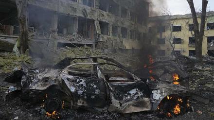 Ein Auto brennt neben einer durch einen Angriff beschädigten Geburtsklinik in Mariupol.