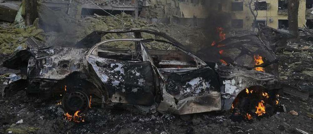 Ein Auto brennt neben einer durch einen Angriff beschädigten Geburtsklinik in Mariupol.