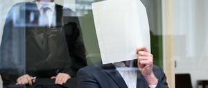 Der Angeklagte sitzt zu Prozessbeginn im Verhandlungssaal im Landgericht München und hält sich einen Bogen Papier vor das Gesicht.