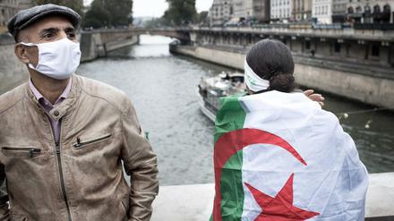 Zwei Personen stehen im Oktober 2020 in Paris an der Seine, eine hat sich die Algerienflagge umgehängt. Sie erinnern an eine Demo im Oktober 1961, bei der mehrere Algerier umgebracht wurden, die gegen den Algerienkrieg demonstrierten.