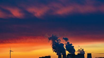 Brandenburg, Jänschwalde: Farbenprächtig leuchten die Wolken im Sonnenuntergang über den Kühltürmen des Braunkohlekraftwerks Jänschwalde der Lausitz Energie Bergbau AG (LEAG) neben dem ein Windrad steht. Die Braunkohle wird im nahen Tagebau Jänschwalde gefördert.