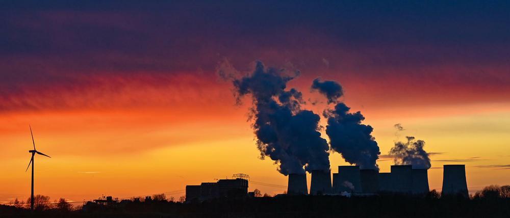Brandenburg, Jänschwalde: Farbenprächtig leuchten die Wolken im Sonnenuntergang über den Kühltürmen des Braunkohlekraftwerks Jänschwalde der Lausitz Energie Bergbau AG (LEAG) neben dem ein Windrad steht. Die Braunkohle wird im nahen Tagebau Jänschwalde gefördert.
