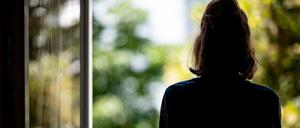 Eine Frau, die ein dunkles T-Shirt trägt, steht an einem offenen Fenster und blickt ins Grüne.
