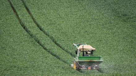 Furchen im Feld. Mit dem Düngerstreuer am Traktor fährt ein Landwirt im Main-Kinzig-Kreis durch noch grünes Getreide.