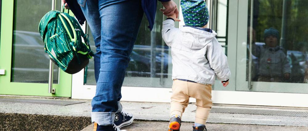 Ein Kind und seine Mutter gehen zum Eingang einer Kita. Mit Beginn der Woche wird für Eltern in Berlin wieder manches einfacher. Bei der Rückkehr zum Regelbetrieb unter Pandemiebedingungen ist aber noch nicht alles wieder so wie vor Corona-Zeiten.