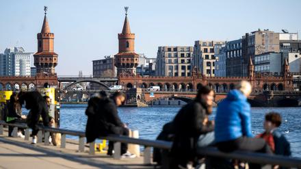 Zahlreiche Menschen genießen das sonnige Wetter am Spreeufer vor der Kulisse der Oberbaumbrücke.