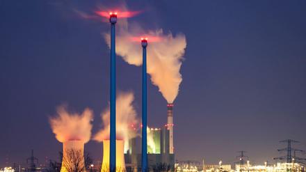 Der Schornstein und die Kühltürme des Braunkohlekraftwerks Schkopau dampfen hinter einem Windpark.