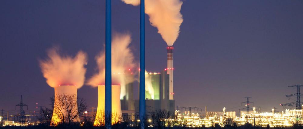 Der Schornstein und die Kühltürme des Braunkohlekraftwerks Schkopau dampfen hinter einem Windpark.