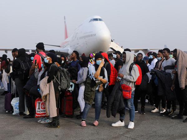 Eine Gruppe von Studierenden steht mit Handgepäck auf dem Flugfeld vor einem Passagierflugzeug.