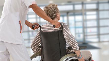 Eine Pflegekraft schiebt eine Seniorin im Rollstuhl. 