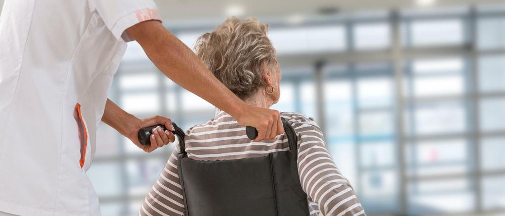 Eine Pflegekraft schiebt eine Seniorin im Rollstuhl. 