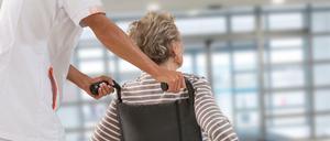 Eine Pflegekraft schiebt eine Seniorin im Rollstuhl. 