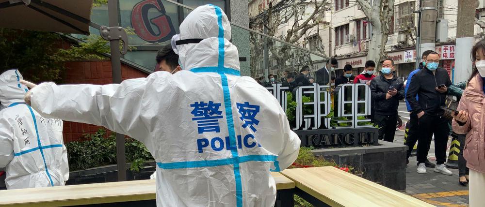 Polizeibeamte in Schutzkleidung führen Anwohner, die sich für Corona-Tests in Shanghai anstellen. 
