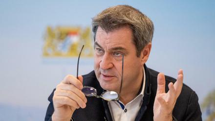Markus Söder, Ministerpräsident von Bayern, sitzt vor Beginn einer Online-Sitzung des bayerischen Kabinetts an seinen Platz vor einer Fotowand. 