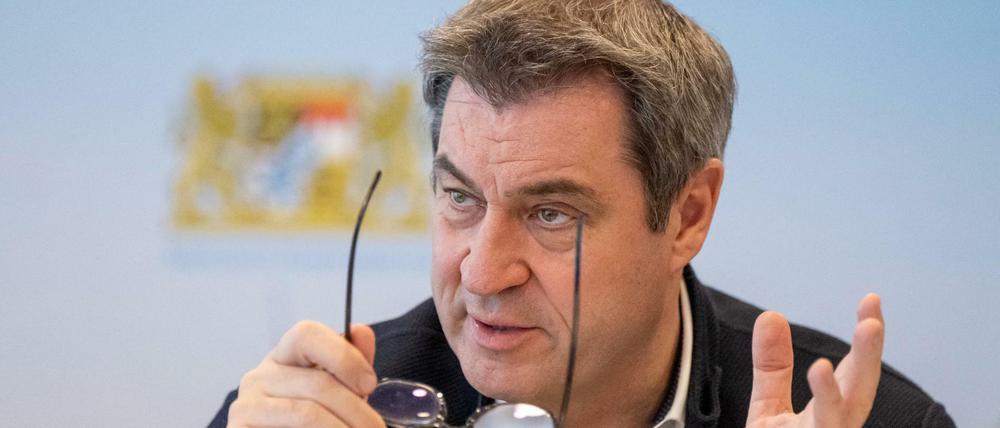 Markus Söder, Ministerpräsident von Bayern, sitzt vor Beginn einer Online-Sitzung des bayerischen Kabinetts an seinen Platz vor einer Fotowand.