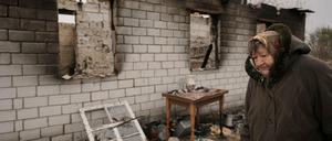 Eine Frau geht an einem Haus vorbei, das während der Besetzung ihres Dorfes durch russische Truppen in Andrijiwka, Ukraine, zerstört wurde.