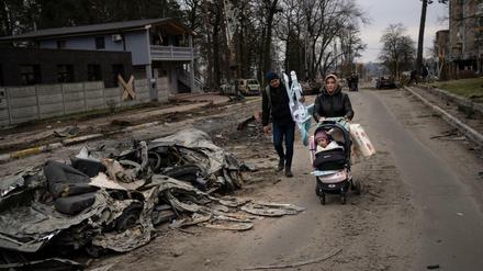Eine Familie geht an einem durch russische Panzer zerstörtem Auto in Butscha vorbei.