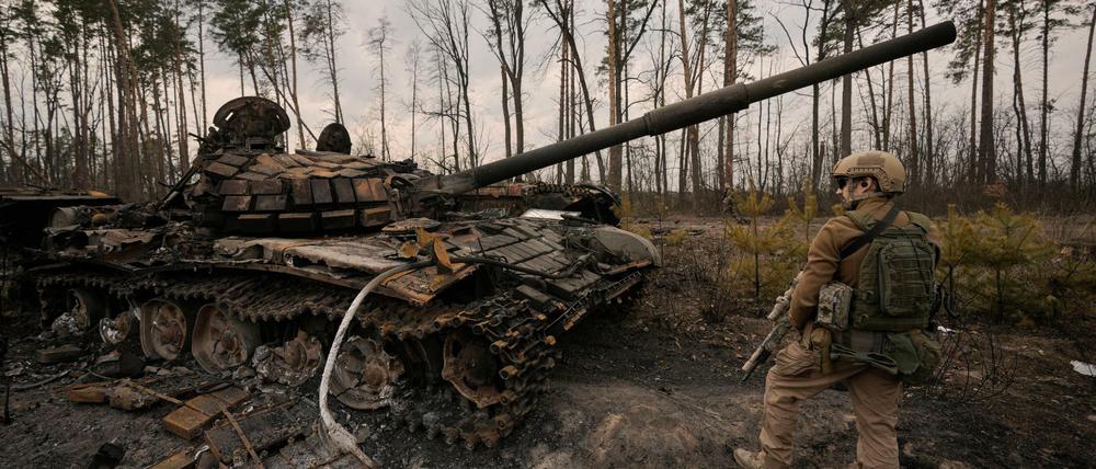Ein ukrainischer Soldat steht neben einem zerstörten Panzer. 