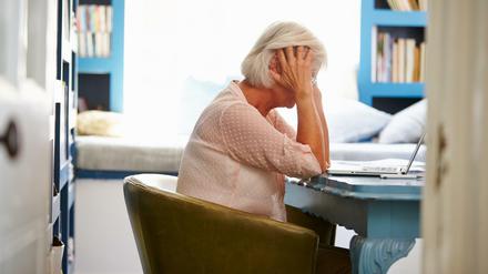 Eine weißhaarige Frau sitzt an einem Tisch und stützt den Kopf mit ihren Händen.