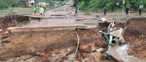 Gestrandete Menschen stehen, nach ungewöhnlich heftigen Niederschlägen, vor einer weggeschwemmten Brücke.