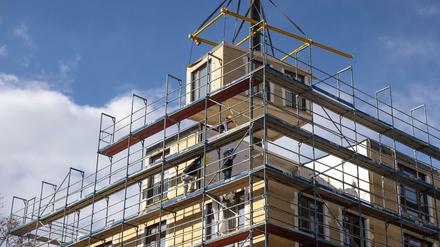 Einzelne Wohneinheiten, die aus Holz und Glas bestehen, werden mit einem Kran von oben auf ein entstehendes Haus gesetzt.