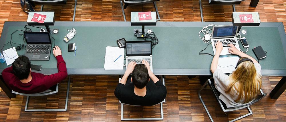 Studierende arbeiten mit ihren Laptops in einer Unibibliothek.