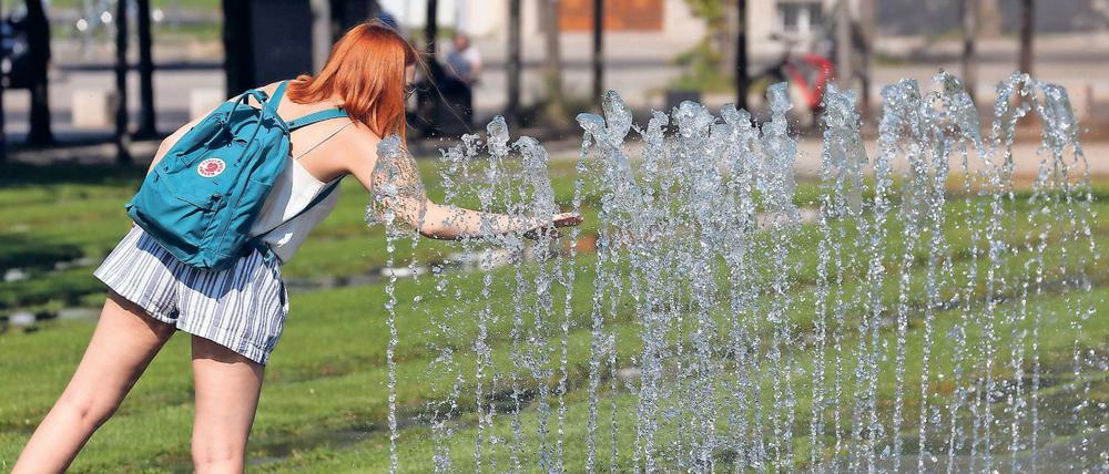 Eine junge Frau erfrischt sich im Sommer am City-Brunnen in Berlin.