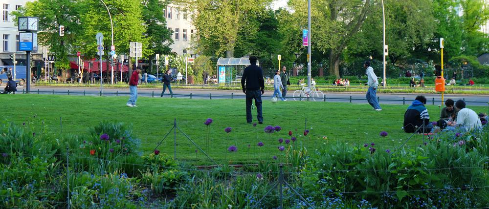 Jugendliche sitzen auf der Grünanlage am Savignyplatz und spielen dort Fußball.