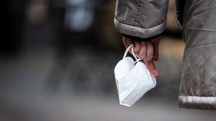 Eine Passantin hält eine Maske in der Hand. Für viele Menschen hat Corona in den vergangenen Monaten seinen Schrecken verloren.
