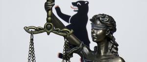 Eine Figur von Justitia steht vor der Länderfahne von Berlin.
