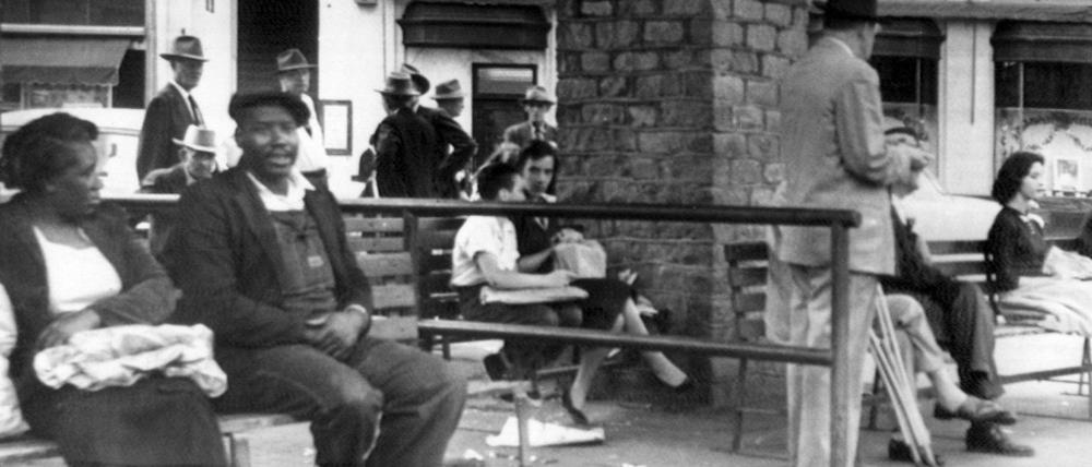 Zwei afroamerikanische US-Bürger an einer Bushaltestelle in Montgomery, Alabama (1956) Sie sind durch eine Barriere von den wartenden Weißen getrennt.