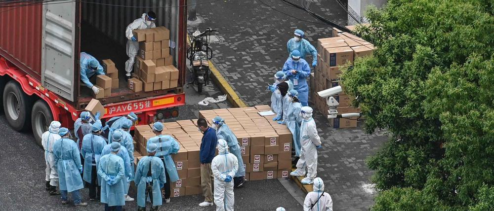 In Shanghai laden Arbeiter in Schutzkleidung einen Truck mit Warenlieferungen aus.