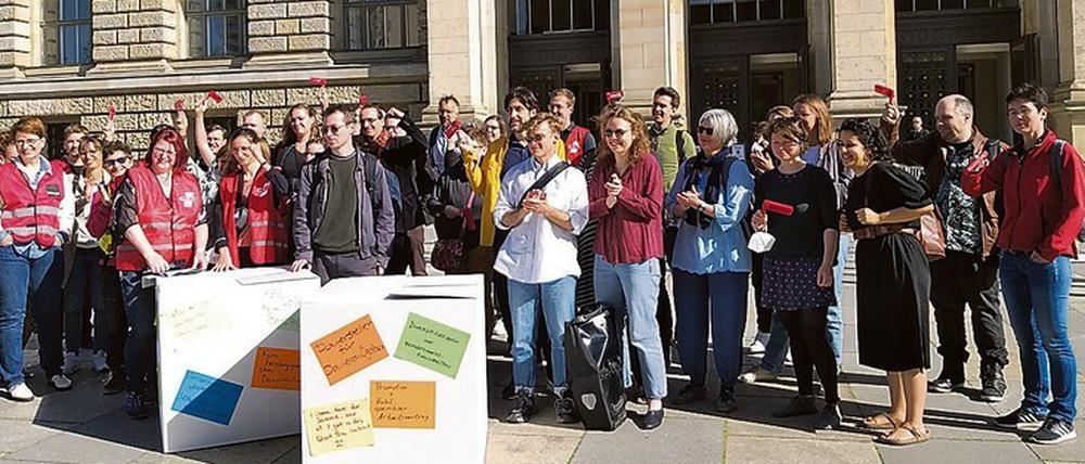 Wissenschaftliche Mitarbeiter:innen stehen in Warnwesten und mit Rasseln vor dem Berliner Abgeordnetenhaus.