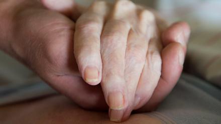 Ein Altenpfleger hält in einem Pflegeheim die Hand einer Frau.