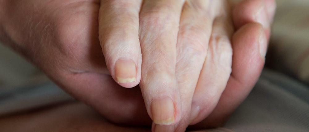 Ein Altenpfleger hält in einem Pflegeheim die Hand einer Frau.