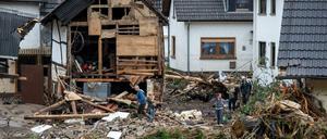 Anwohner gehen in dem Ort im Kreis Ahrweiler nach dem Unwetter mit Hochwasser durch den Schutt an einem beschädigten Gebäude vorbei.