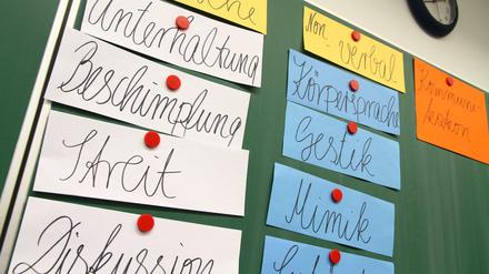 An einer Schultafel hängen Zettel mit Begriffen wie Gestik, Streit, Diskussion oder Körpersprache.