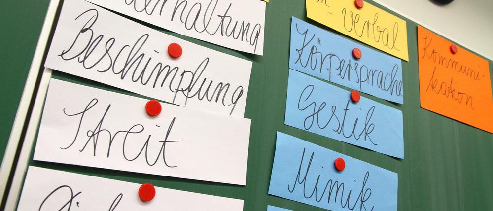 An einer Schultafel hängen Zettel mit Begriffen wie Gestik, Streit, Diskussion oder Körpersprache.