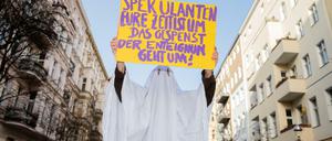 Eine Aktivistin im Gespensterkostüm hält ein Protestschild nahe dem Organisationsbüro des Volksbegehrens ´Deutsche Wohnen &amp; Co. enteignen» in die Kamera. 