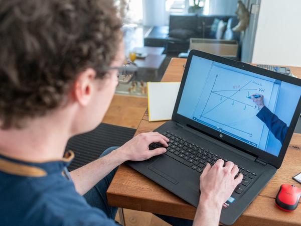 Ein Student sitzt in seinem WG-Zimmer an einem Laptop und schaut sich ein Tutorial an.