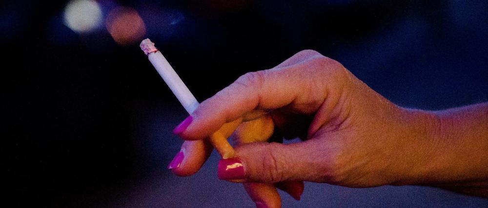 Eine Frau steht auf einer Straße und hält eine Zigarette in der Hand.