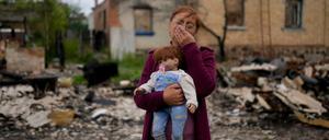 Eine Frau mit der Puppe ihrer Enkelin vor einem zerstörten Haus nahe Kiew