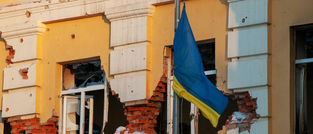 Eine ukrainische Flagge weht vor einem durch Beschuss beschädigten Gebäude.