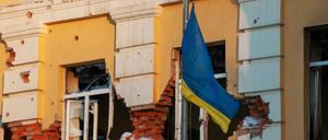 Eine ukrainische Flagge weht vor einem durch Beschuss beschädigten Gebäude.