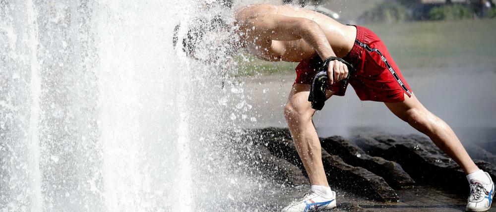 Ein Passant erfrischt sich im Brunnen im Lustgarten bei hohen Temperaturen.