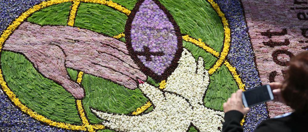 Baden-Württemberg, Hüfingen: Eine Frau fotografiert an Fronleichnam während der Prozession Kirchenmotive in einem Blumenteppich (Archivbild).